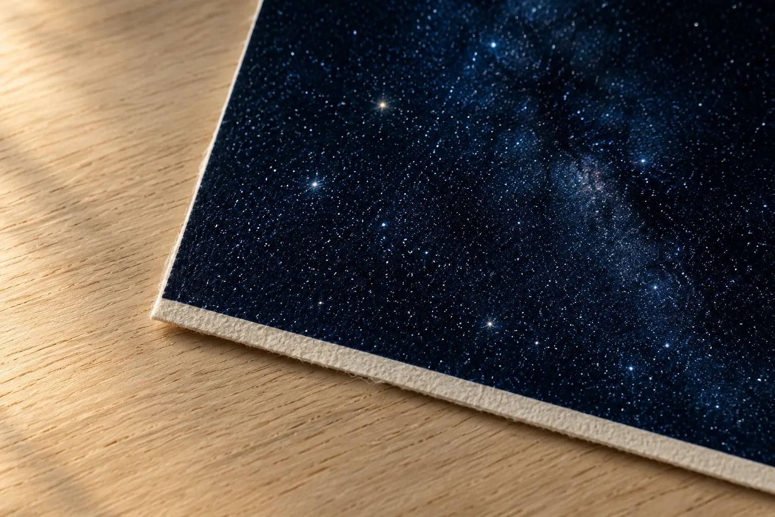 Close-up of the corner of an unframed sheet of matte off-white paper printed with a dark star field to its edge.
