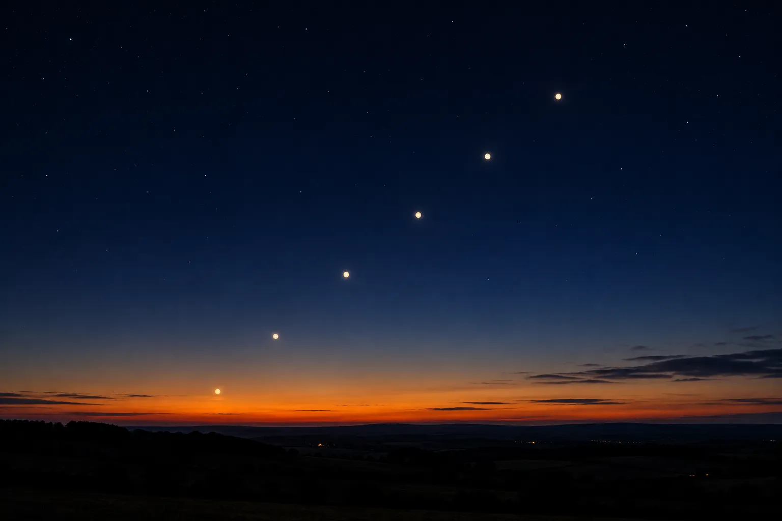 Several bright planets strung along a line above a dark horizon at dusk.