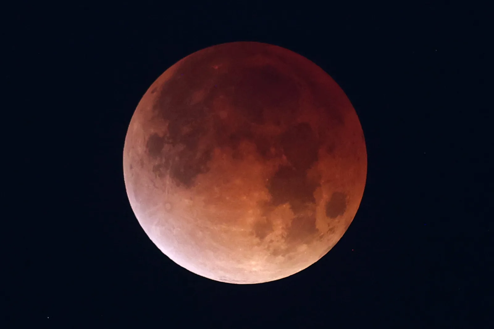 The Moon fully eclipsed, a deep copper red disc against a dark sky.