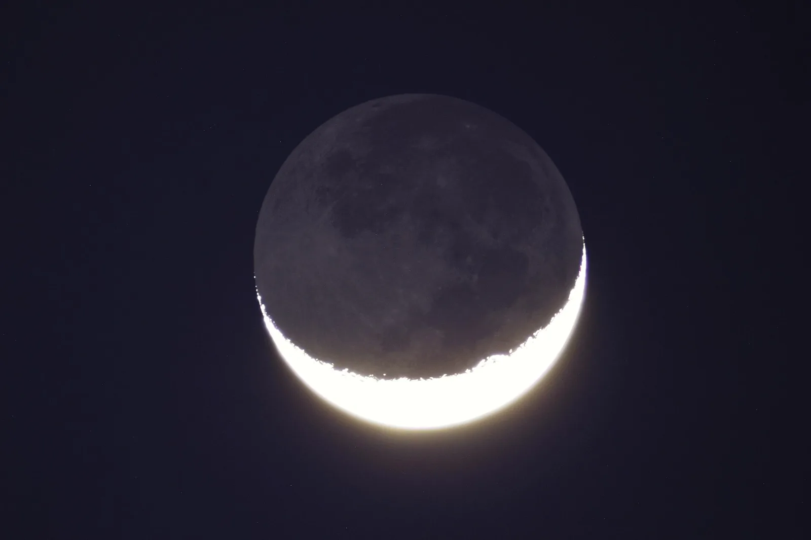 A thin crescent Moon with the rest of its disc faintly visible.