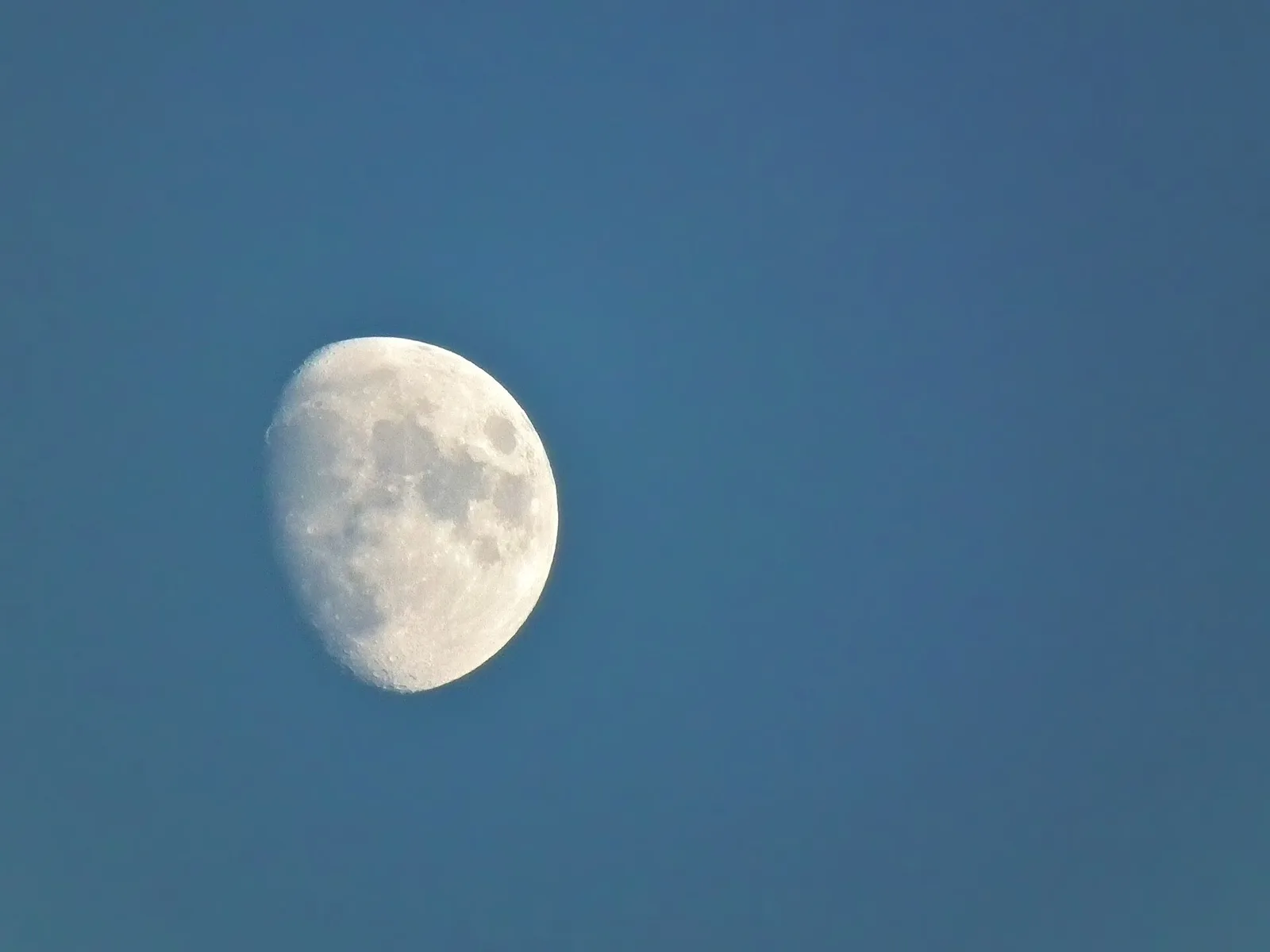 A waxing gibbous Moon, more than half lit, in a blue evening sky.