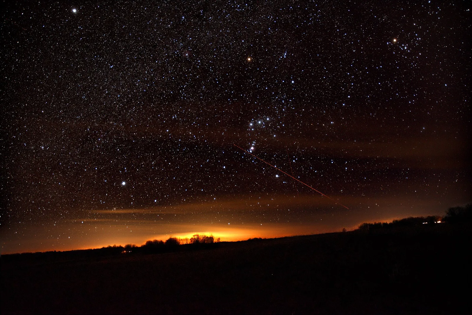 The stars of Orion over a dark horizon with an orange glow along it.
