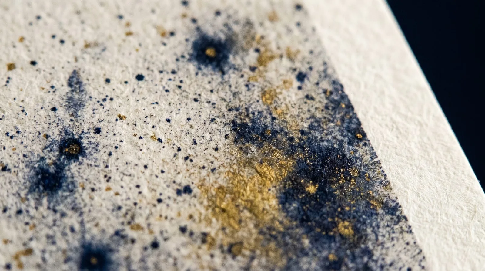A macro view across the surface of a printed sheet: navy and gold ink dots sitting in the fibres of textured off-white paper.