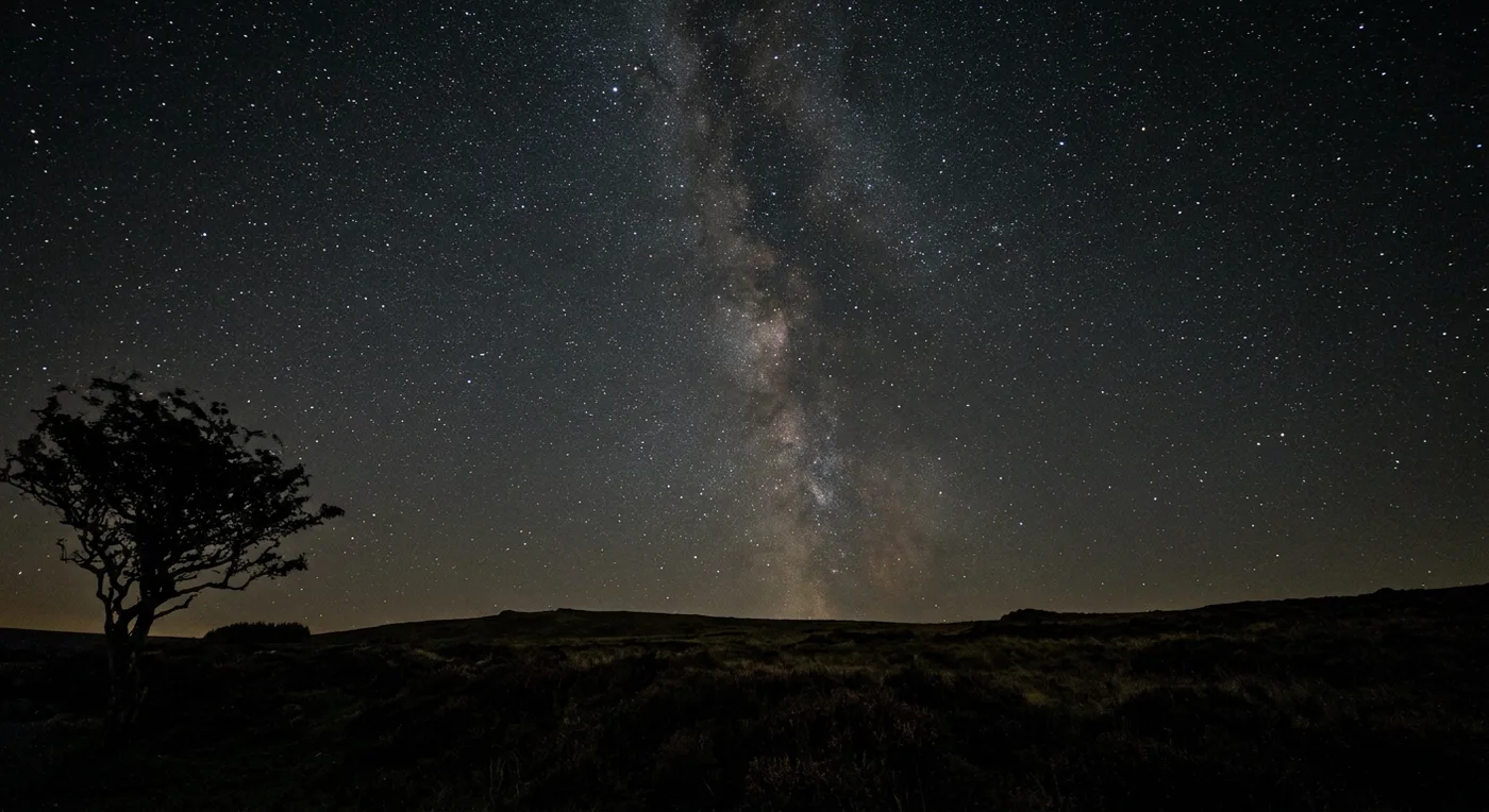 A handheld photograph of a star-filled night sky over dark moorland