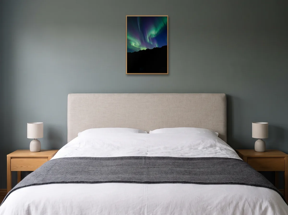 Aurora as an A2 print in a natural wood frame on a sage-grey bedroom wall above a headboard.