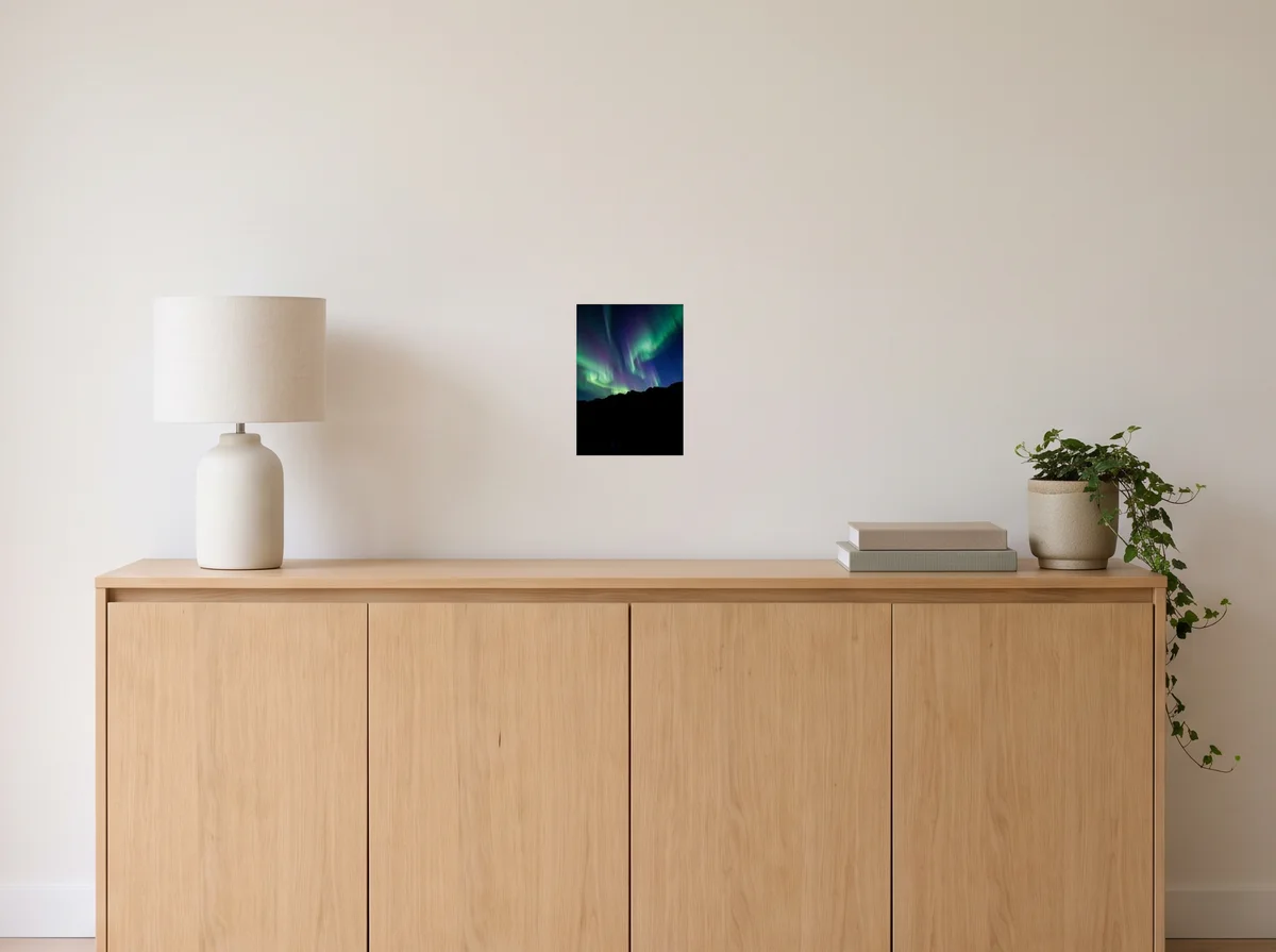 Aurora as an A4 poster on an off-white wall above an oak sideboard with a lamp and plant