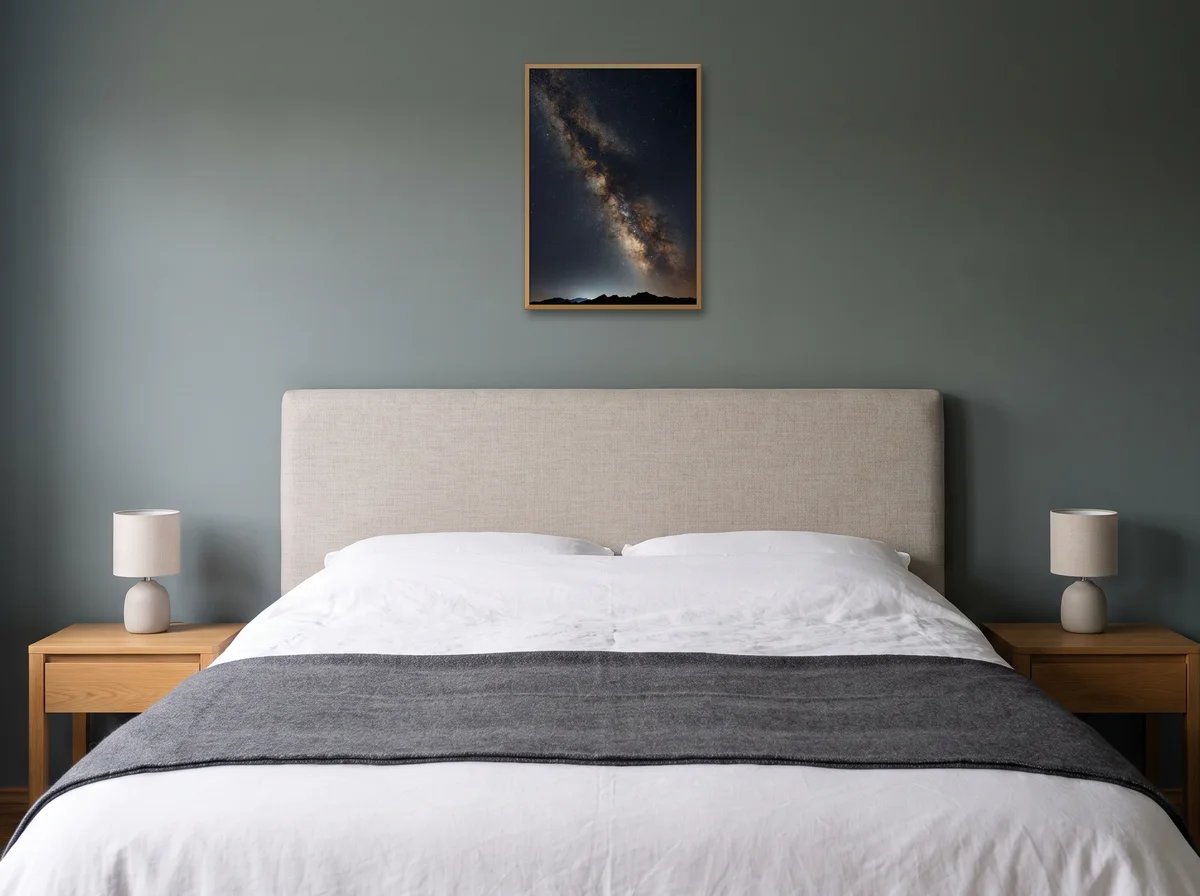 Galactic Core as an A2 print in a natural wood frame on a sage-grey bedroom wall above an upholstered headboard.