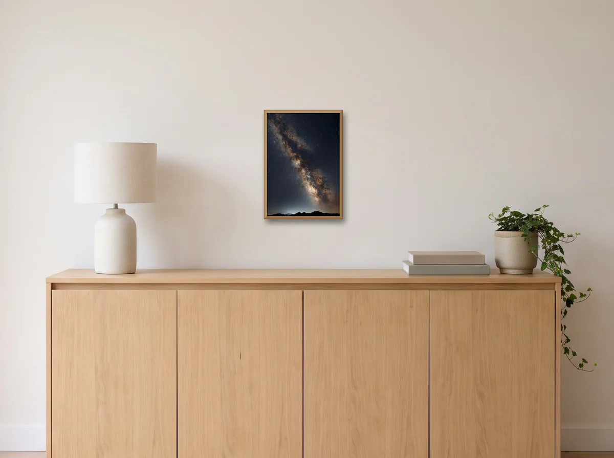 Galactic Core as an A3 poster in a natural wood frame on an off-white wall above an oak sideboard with a lamp and plant