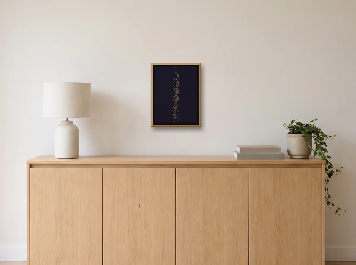 Lunar Phases as a 30x40 cm canvas in a natural wood float frame on an off-white wall above an oak sideboard with a lamp and plant