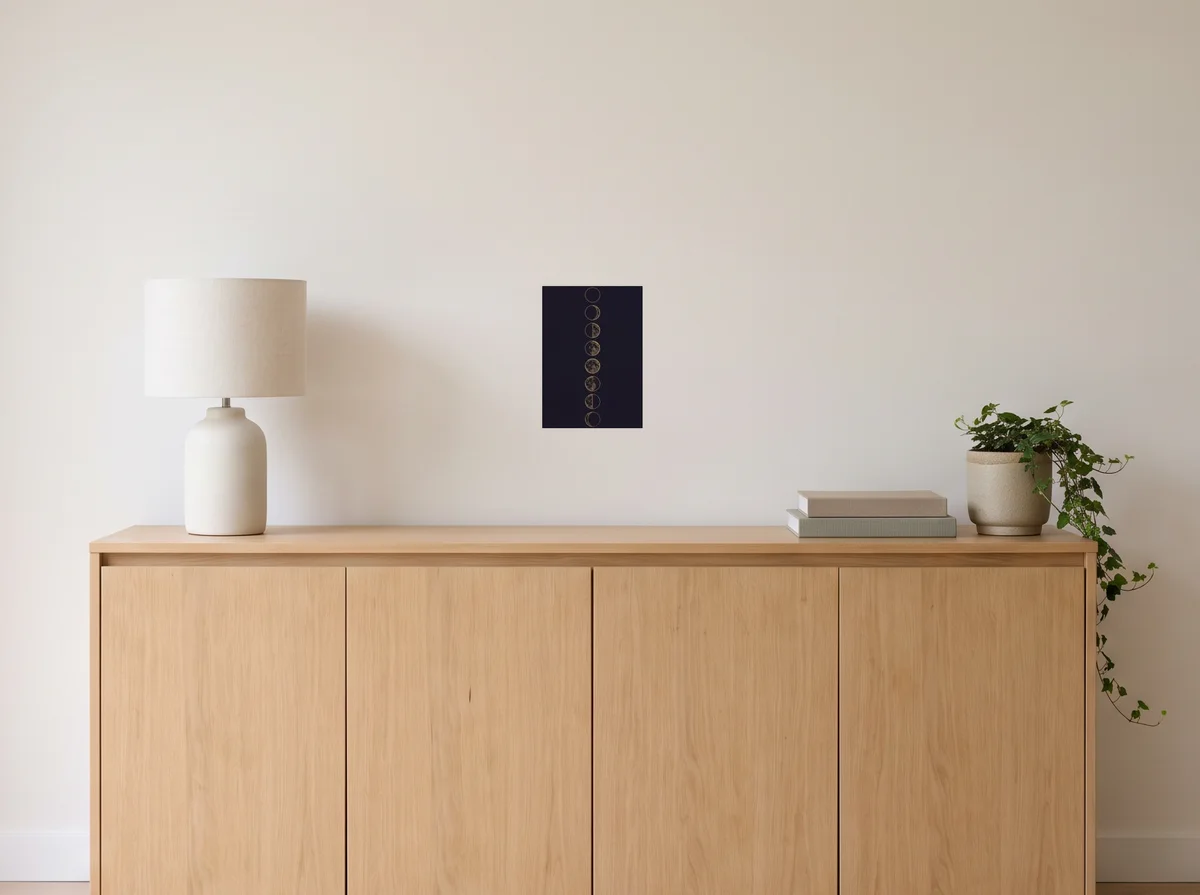 Lunar Phases as an A4 poster on an off-white wall above an oak sideboard with a lamp and plant.