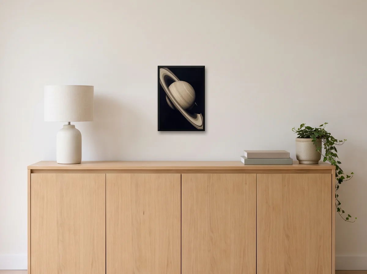 Saturn as an A3 poster in a black frame on an off-white wall above an oak sideboard with a lamp and plant