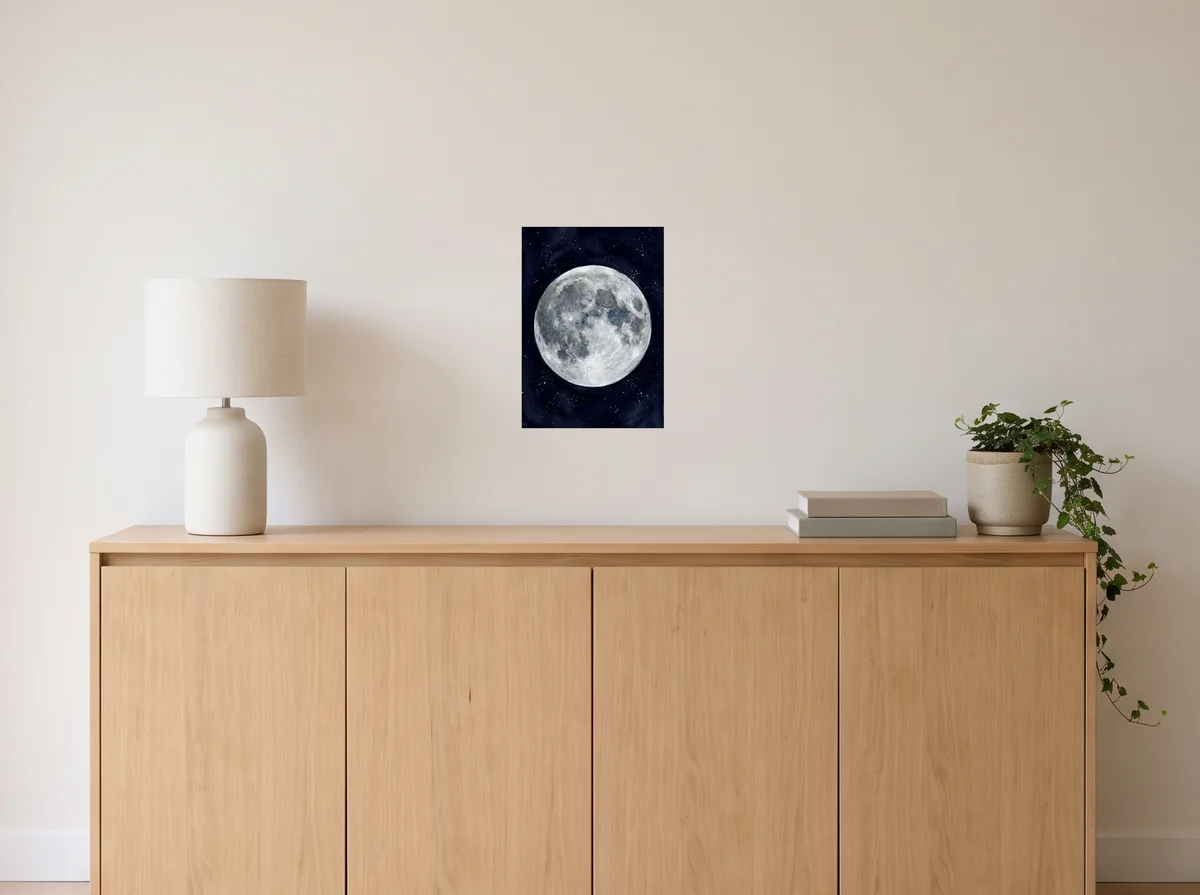 Watercolour Moon as an A3 poster on an off-white wall above an oak sideboard with a lamp and plant
