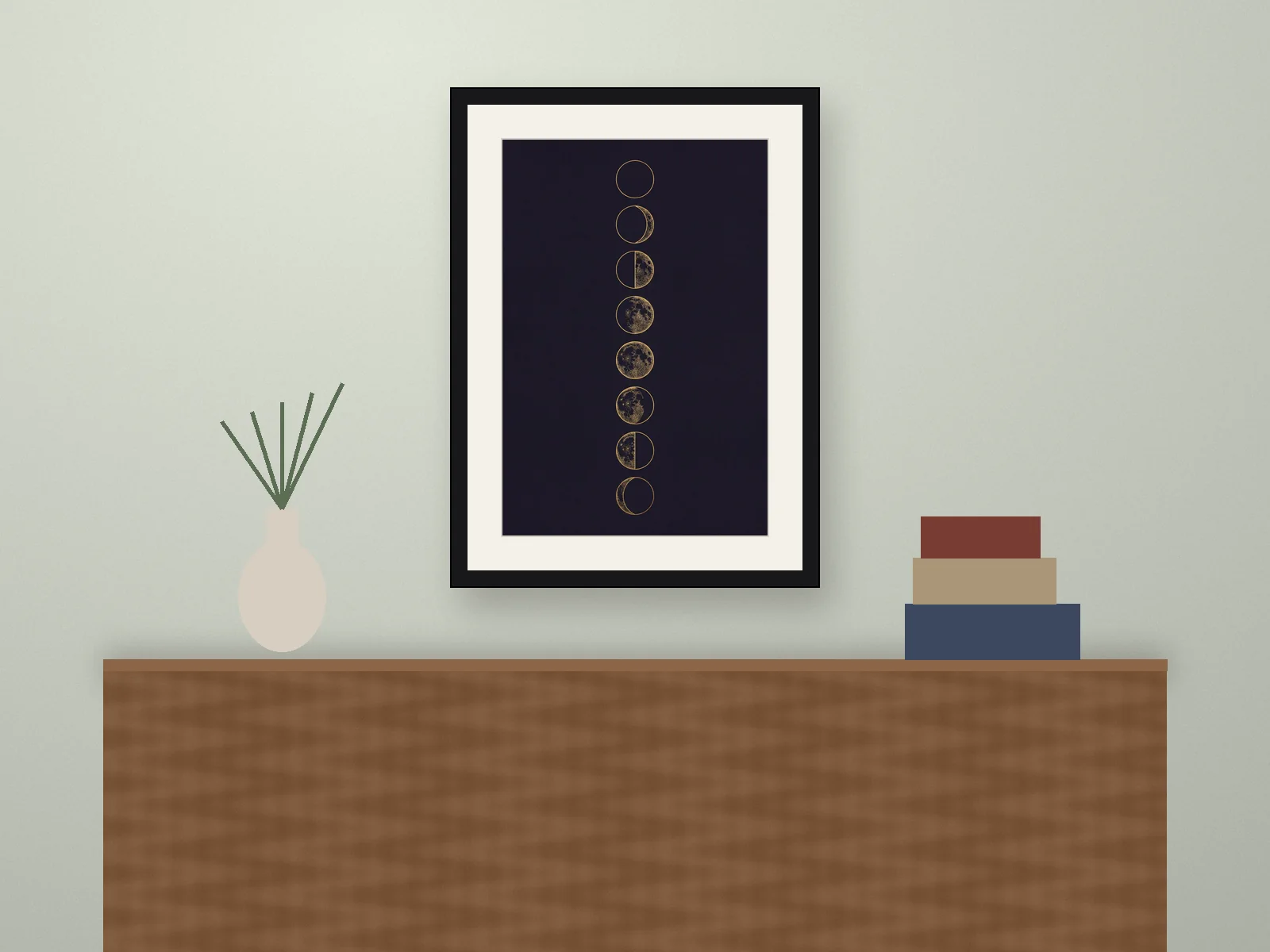 Room mockup: a moon phases print in a black frame above a wooden sideboard, on a sage green wall.